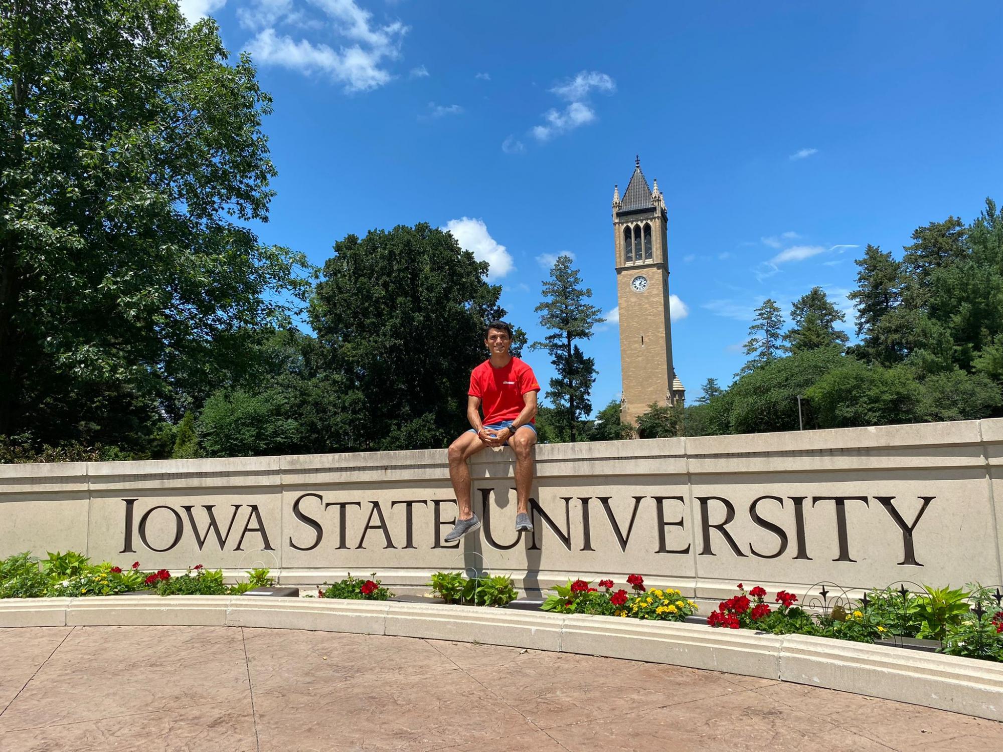 Ezequial sitting on the Iowa State University wall with the campanile in the background